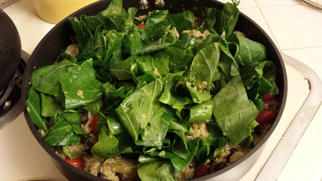skillet filled with leafy kale, quinoa, tomatoes, carmelized onion